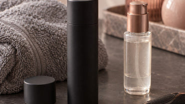 A matte black unbranded cylindrical canister with a cap beside a grey towel