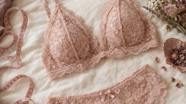 A blush lace bralette and matching set laid out on a bed next to a soft measuring tape