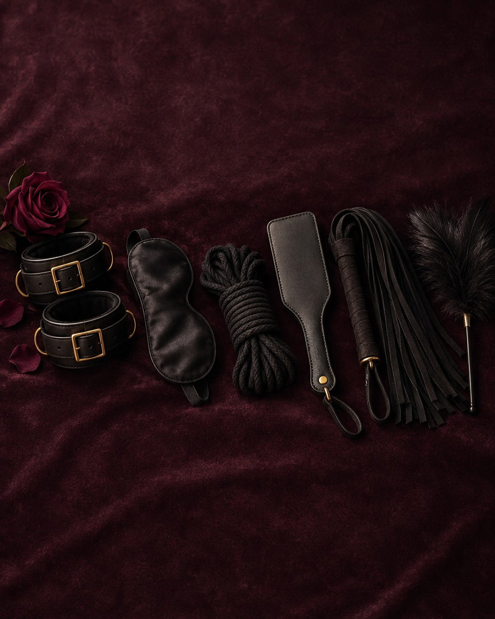 Leather cuffs, blindfold, rope, paddle, flogger and feather on plum velvet